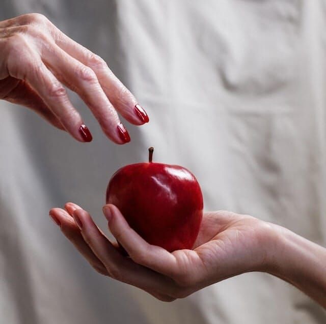 maçã na palma da mão de alguém e outra mão pegando representando tentação