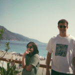 Pai e filha posam para foto analógica em um mirante de uma praia, eles estão felizes.
