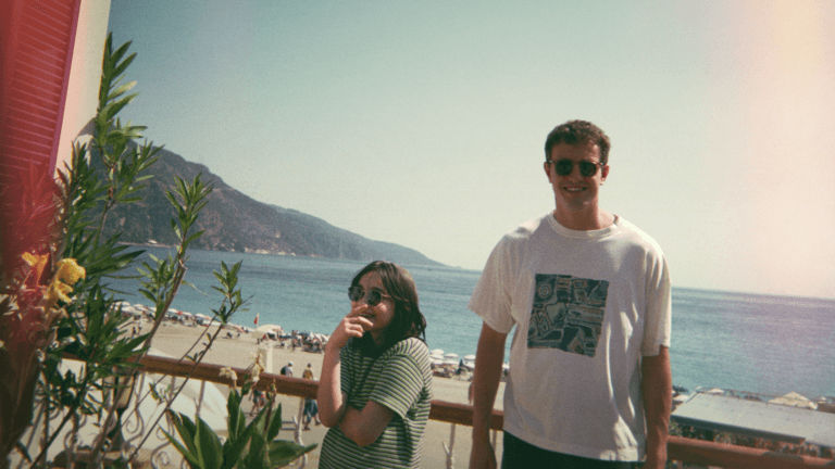 Pai e filha posam para foto analógica em um mirante de uma praia, eles estão felizes.