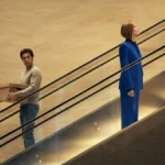 Homem olha para mulher em escada rolante em sentidos contrários em cena do filme Primeiro das Damas da Netflix (1)