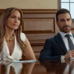 Jennifer Lopez e Brett Goldstein sentados em um tribunal em cena do filme Paixão de Escritório da Netflix de 2026
