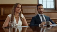 Jennifer Lopez e Brett Goldstein sentados em um tribunal em cena do filme Paixão de Escritório da Netflix de 2026