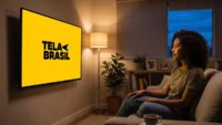 Mulher negra assistindo ao streaming Tela Brasil em TV na sala sentada no sofá
