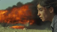 ônibus pega fogo e mulher fica parada assustada em cena do filme Incêndios de 2010