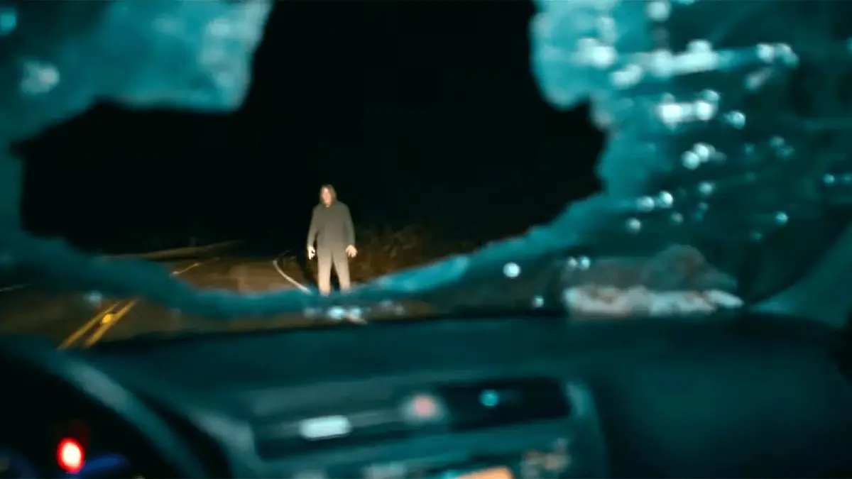 vidro dianteiro de carro quebrado com homem iluminado na estrada em cena do filme de terror Passageiro do Mal de 2026